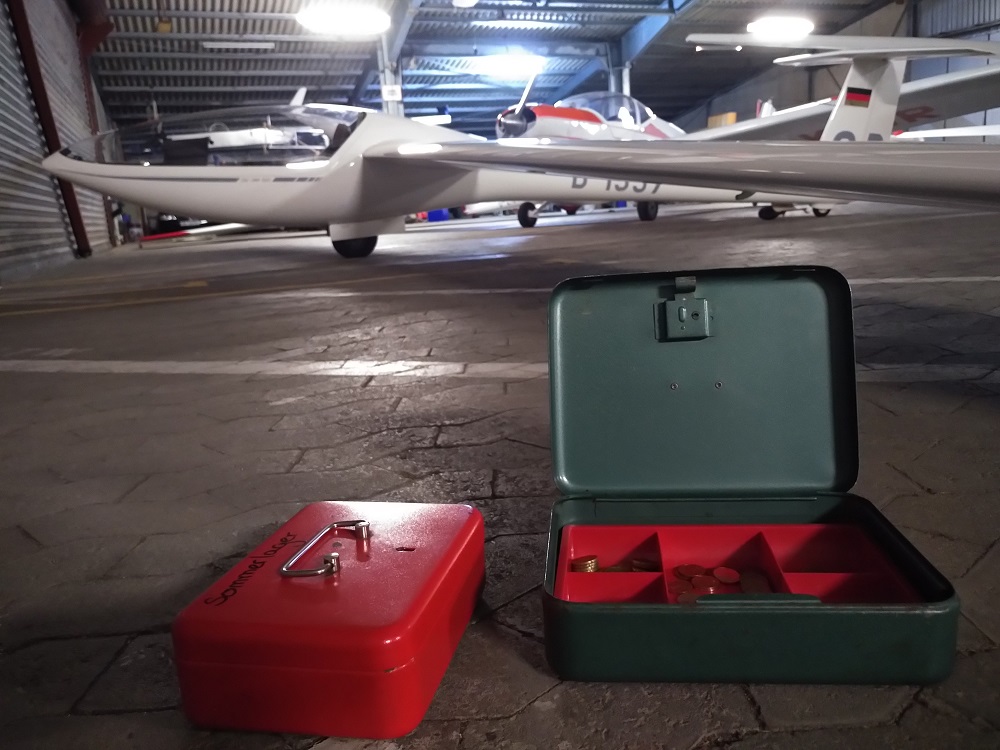 Zwei Kassen auf dem Boden vor einem Seegelflugzeug im Flugzeughangar